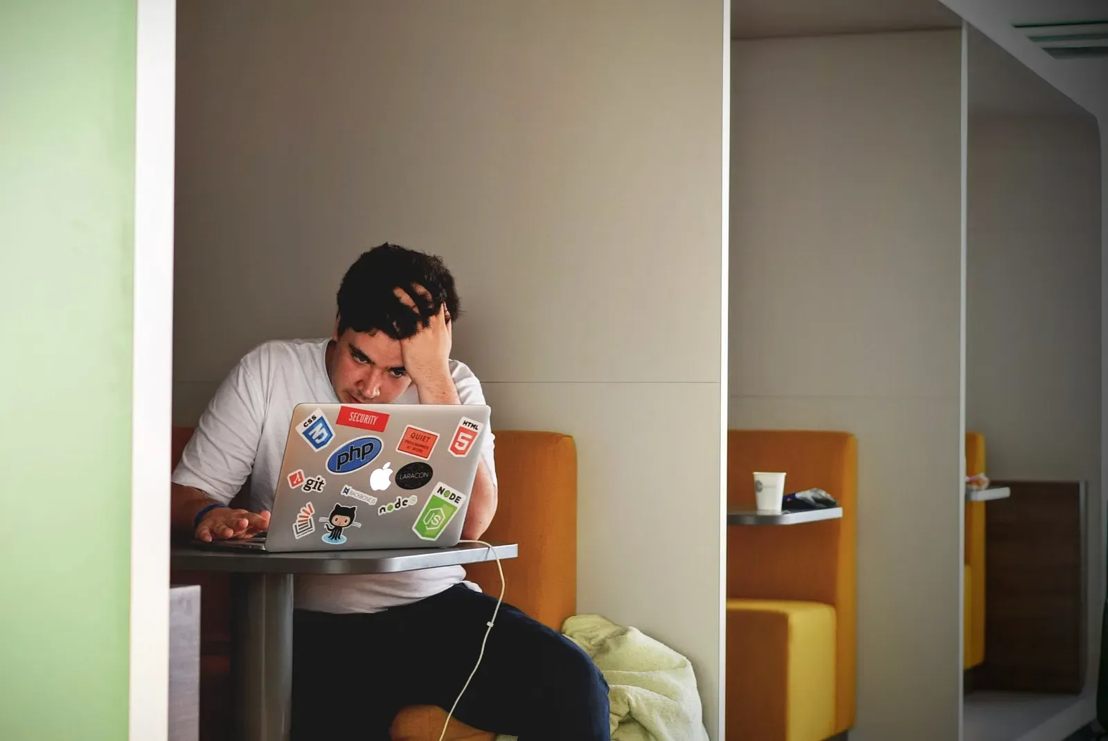 Man at a laptop covered in stickers, holding his head in frustration